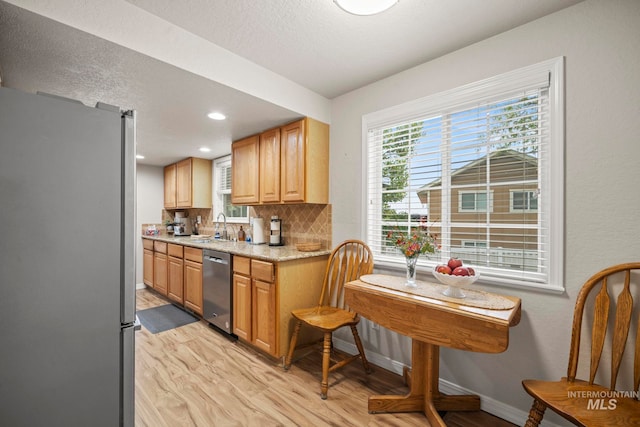 kitchen featuring light stone countertops, a sink, tasteful backsplash, light wood-type flooring, and appliances with stainless steel finishes