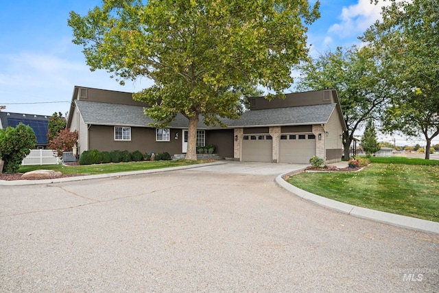 ranch-style house featuring a garage, a front lawn, concrete driveway, and roof with shingles