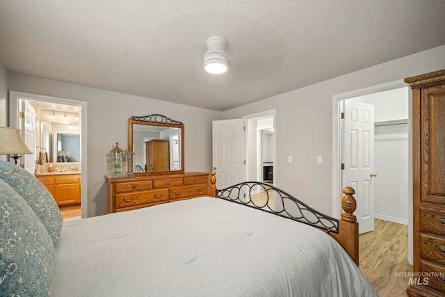 bedroom with connected bathroom, light wood-type flooring, a textured ceiling, and a walk in closet