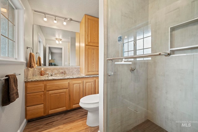 full bathroom with decorative backsplash, a stall shower, toilet, wood finished floors, and vanity