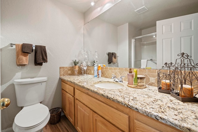 bathroom featuring decorative backsplash, toilet, wood-type flooring, vanity, and walk in shower