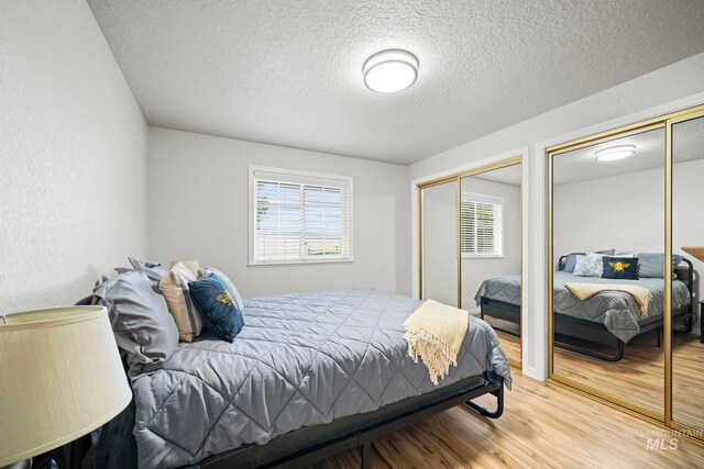 bedroom with wood finished floors, two closets, and a textured ceiling