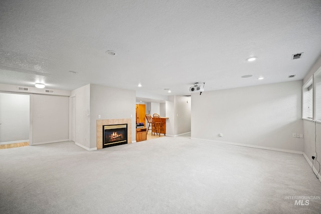 unfurnished living room with a textured ceiling, light carpet, and a tiled fireplace