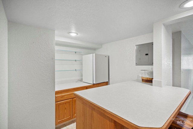 kitchen with a textured wall, light countertops, electric panel, freestanding refrigerator, and a peninsula