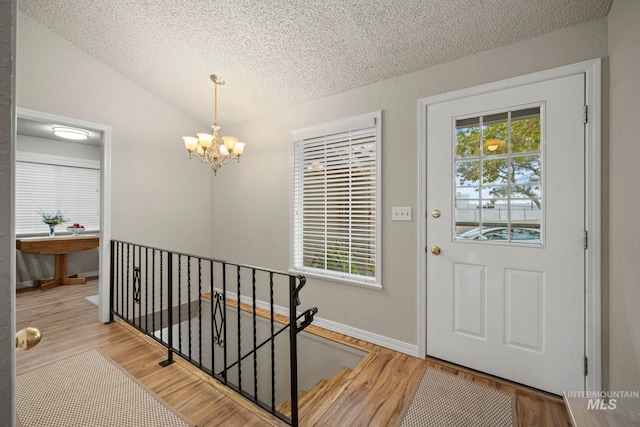 entryway featuring light hardwood / wood-style floors, a textured ceiling, lofted ceiling, and a chandelier