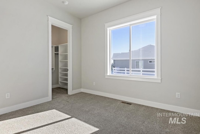 unfurnished bedroom with a walk in closet, carpet, baseboards, visible vents, and a closet