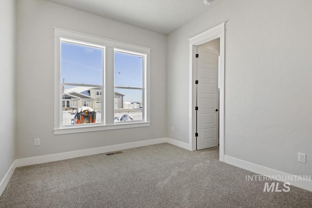 carpeted empty room featuring baseboards, visible vents, and a wealth of natural light