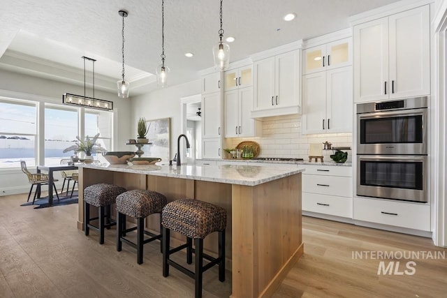 kitchen with recessed lighting, a kitchen island with sink, stainless steel double oven, and light wood-style flooring