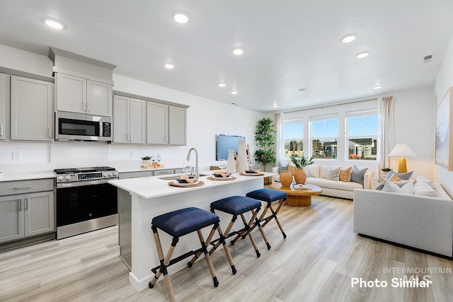 kitchen featuring sink, gray cabinetry, stainless steel appliances, an island with sink, and a kitchen bar