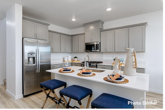 kitchen with appliances with stainless steel finishes, sink, a breakfast bar area, gray cabinetry, and light wood-type flooring