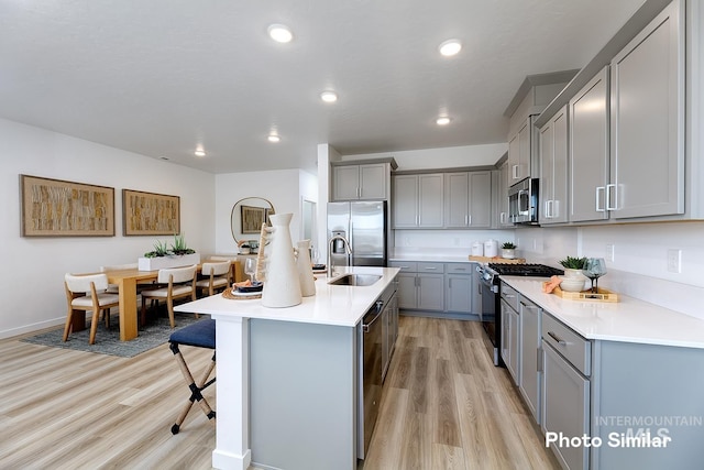 kitchen with appliances with stainless steel finishes, sink, a kitchen bar, a kitchen island with sink, and light hardwood / wood-style floors