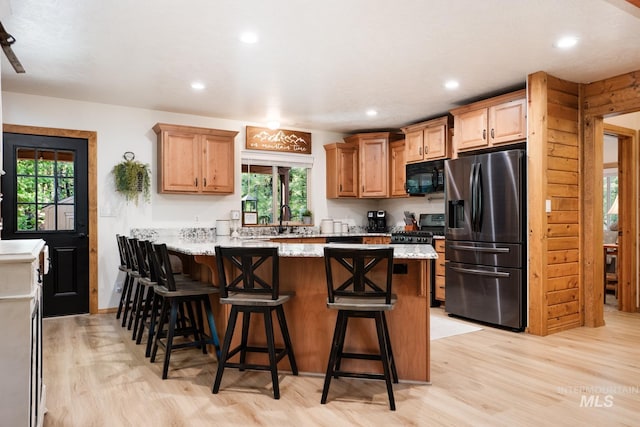 kitchen featuring stainless steel fridge with ice dispenser, black microwave, a peninsula, light wood-style flooring, and a kitchen bar