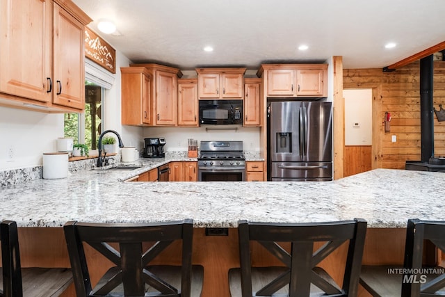 kitchen with stainless steel appliances, a sink, light stone counters, a peninsula, and recessed lighting