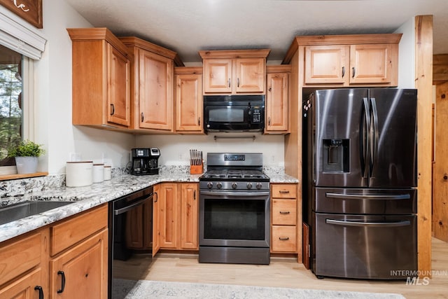 kitchen featuring black appliances, light wood-type flooring, and light stone countertops