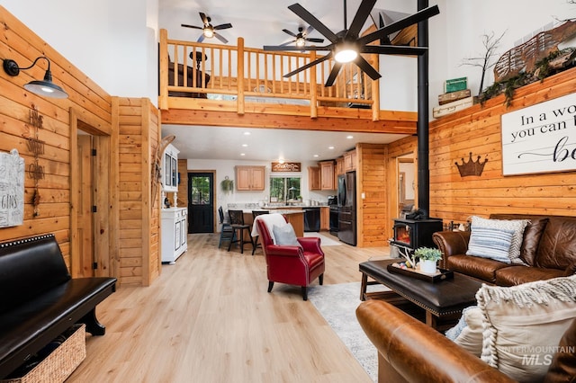 living room with a towering ceiling, a wood stove, light wood finished floors, ceiling fan, and recessed lighting