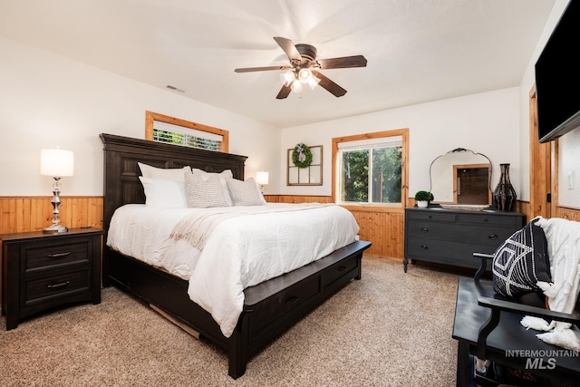bedroom with wood walls, a wainscoted wall, light carpet, and a ceiling fan
