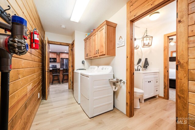 clothes washing area with independent washer and dryer, light wood finished floors, and cabinet space