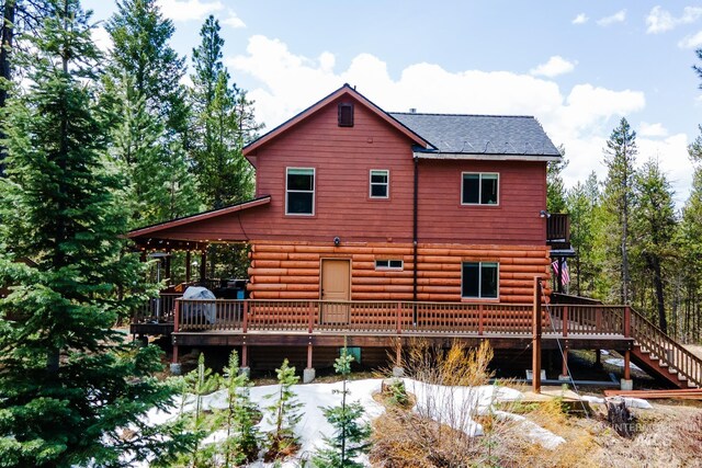 rear view of property featuring a deck, log exterior, stairs, and roof with shingles