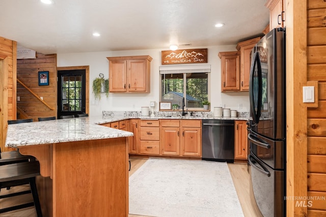 kitchen featuring dishwasher, freestanding refrigerator, a peninsula, a sink, and light wood-type flooring