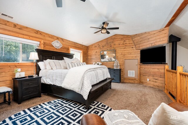 carpeted bedroom featuring wood walls, multiple windows, vaulted ceiling, and a ceiling fan