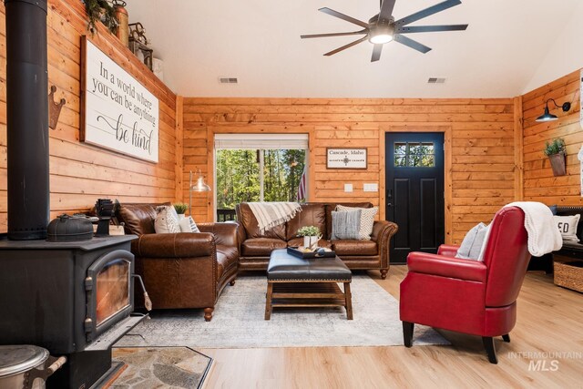living area with a wood stove, vaulted ceiling, ceiling fan, wood walls, and wood finished floors