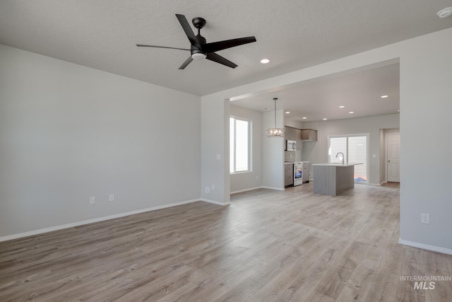 unfurnished living room featuring light wood finished floors, a wealth of natural light, baseboards, and a ceiling fan