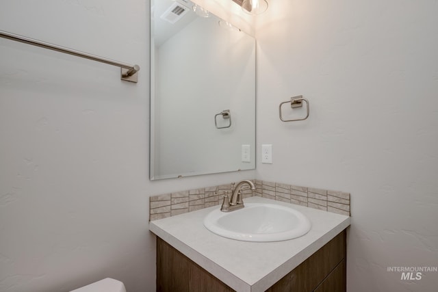 half bathroom with vanity, toilet, and visible vents