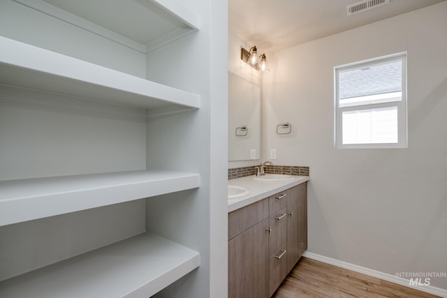 full bathroom with baseboards, visible vents, a sink, double vanity, and wood finished floors