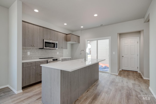 kitchen with a sink, stainless steel appliances, tasteful backsplash, light countertops, and light wood-style floors