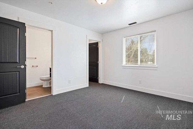 unfurnished bedroom with ensuite bath and dark carpet