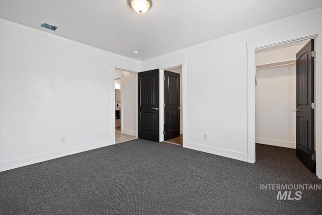 unfurnished bedroom featuring a spacious closet, a closet, and dark colored carpet