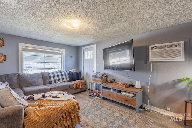 living area featuring baseboards, a textured ceiling, an AC wall unit, and wood finished floors