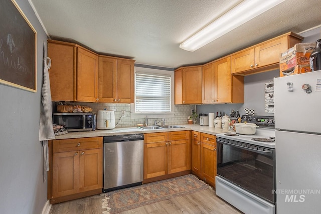 kitchen with a sink, appliances with stainless steel finishes, light wood-style flooring, and light countertops