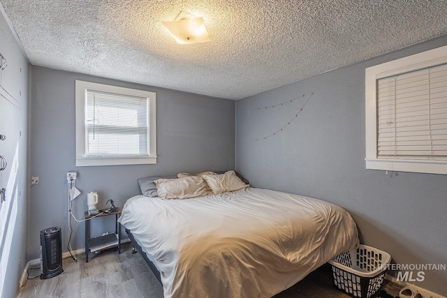 bedroom with a textured ceiling, baseboards, and wood finished floors