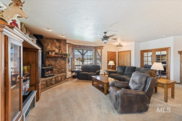 living room featuring ceiling fan, a wood stove, light carpet, and a textured ceiling