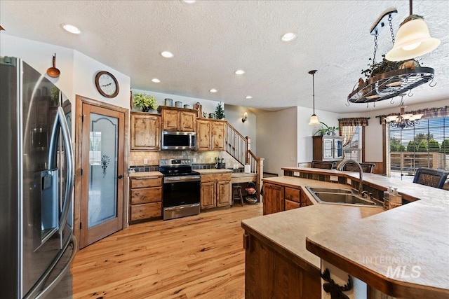 kitchen with appliances with stainless steel finishes, sink, decorative backsplash, hanging light fixtures, and light hardwood / wood-style floors