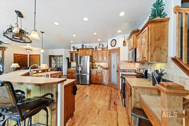 kitchen with sink, appliances with stainless steel finishes, backsplash, a kitchen breakfast bar, and decorative light fixtures