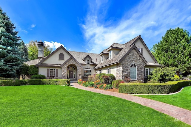 view of front facade featuring a chimney, a front lawn, stucco siding, and stone siding