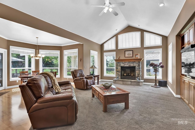 living area with light carpet, a stone fireplace, baseboards, ceiling fan with notable chandelier, and vaulted ceiling