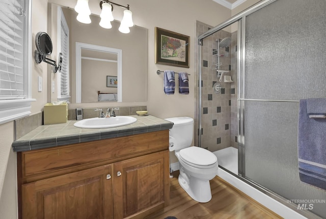 bathroom with a shower stall, wood finished floors, vanity, toilet, and ornamental molding
