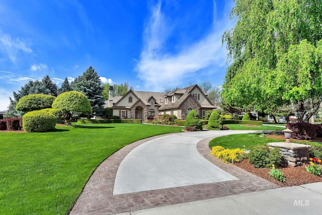 view of front of house with stone siding, curved driveway, a chimney, and a front yard