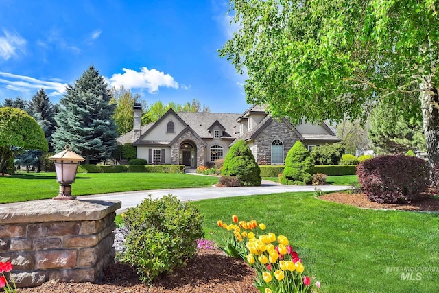 tudor house with stucco siding, a chimney, stone siding, and a front lawn