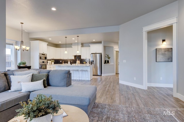 living room featuring light wood-style floors, a chandelier, baseboards, and recessed lighting