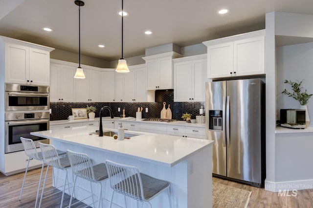 kitchen with appliances with stainless steel finishes, a sink, backsplash, light wood finished floors, and recessed lighting