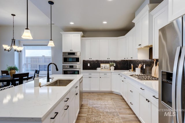 kitchen featuring appliances with stainless steel finishes, a sink, a center island with sink, light wood-type flooring, and a chandelier