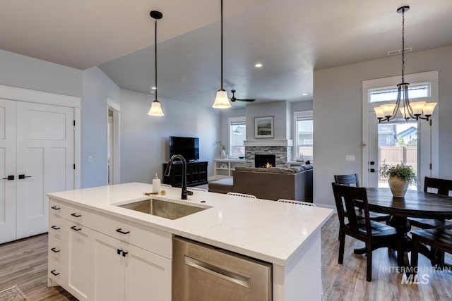 kitchen with stainless steel dishwasher, a sink, light wood finished floors, a fireplace, and recessed lighting