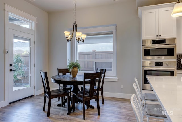 dining space featuring light wood-style flooring, a chandelier, and baseboards
