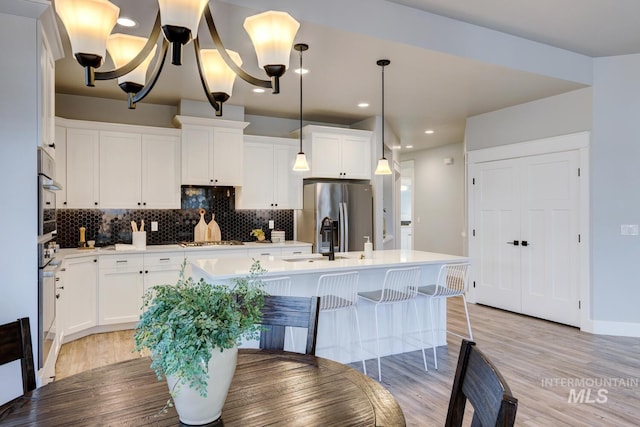 kitchen with appliances with stainless steel finishes, decorative backsplash, light countertops, an island with sink, and recessed lighting