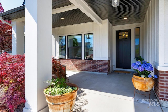 doorway to property featuring brick siding, a porch, and board and batten siding