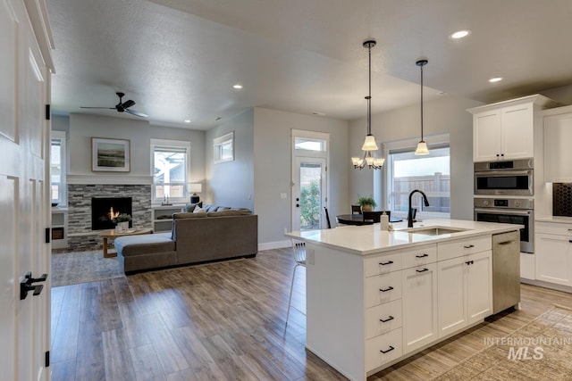 kitchen with a sink, open floor plan, a stone fireplace, light wood-style floors, and ceiling fan